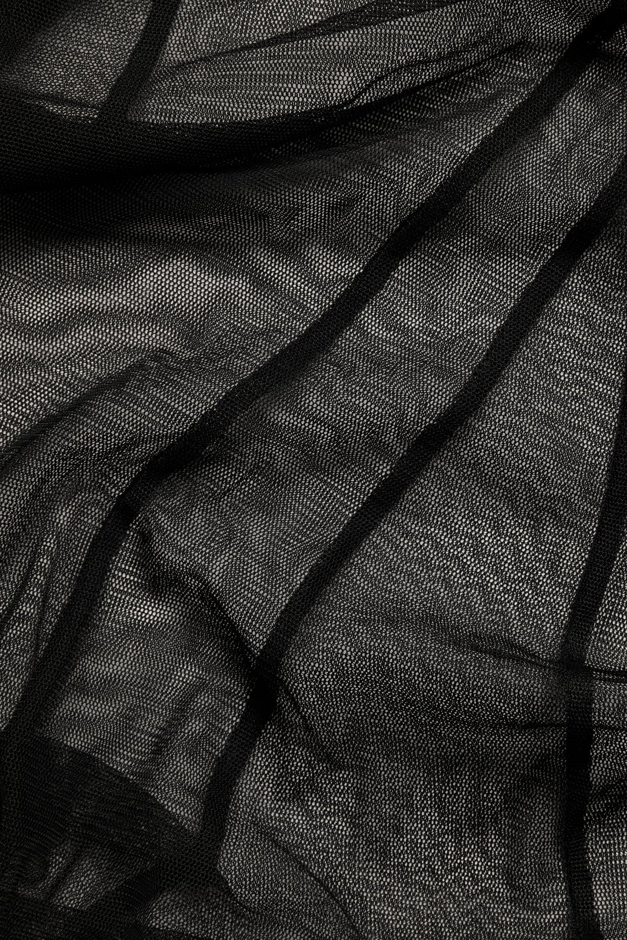 Zbliżenie czarnej siateczkowej tkaniny poliestrowej na długą spódnicę, ukazujące jej przezroczystą teksturę i fałdy.