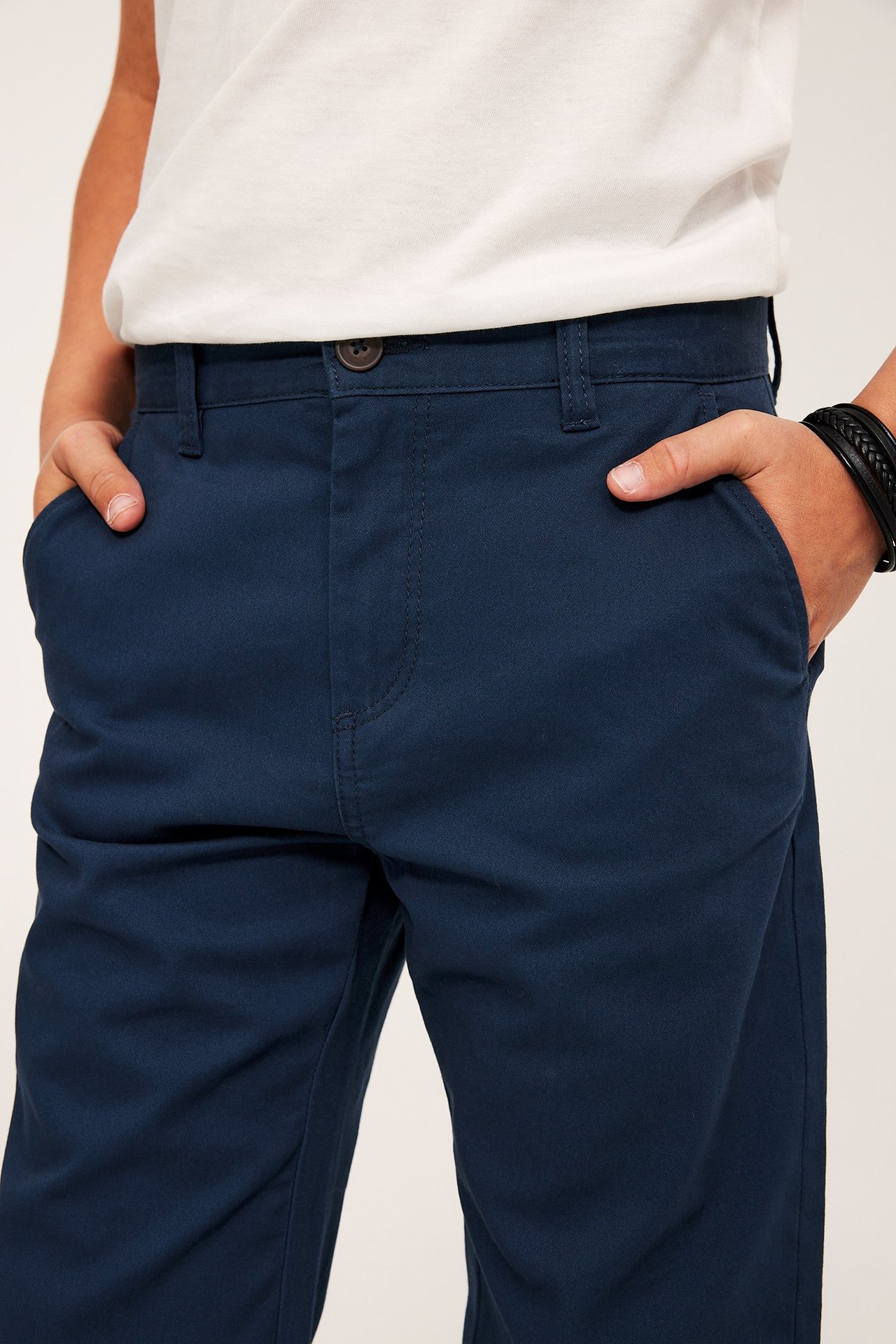 Lapsi, tummansiniset joustavat chinot, edestä, nappi ja vetoketju.