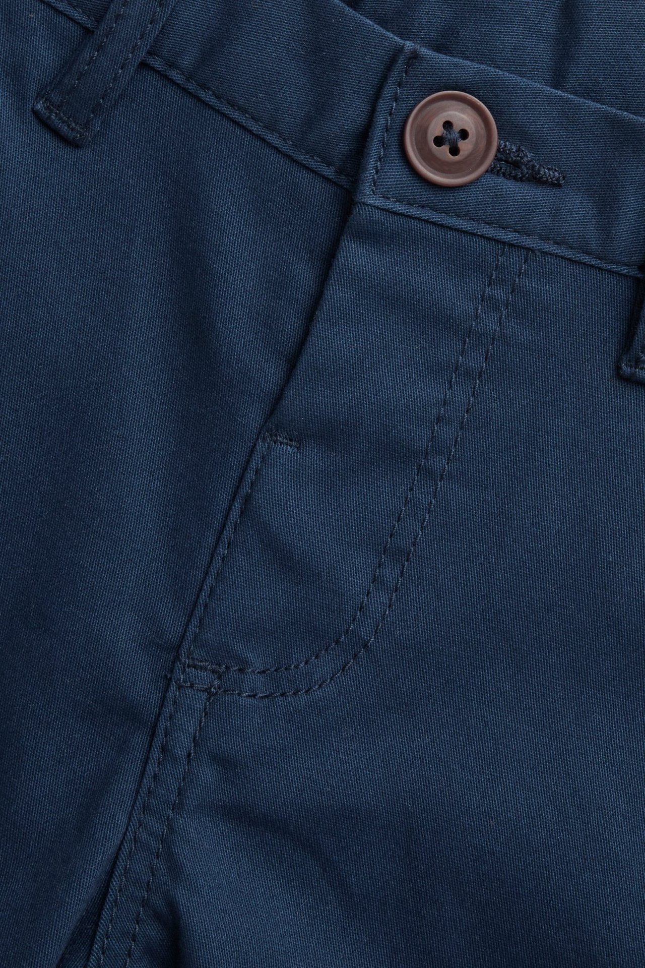 Zbliżenie na ciemnoniebieskie chinosy dziecięce z mieszanki bawełny z brązowym guzikiem i zamkiem.