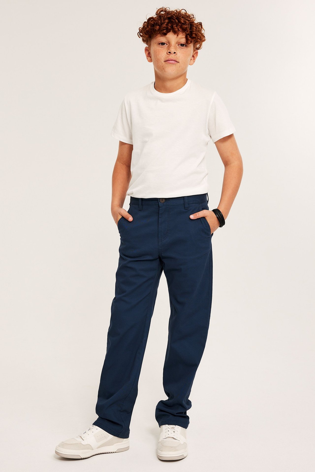 Poika valkoisessa T-paidassa ja tummansininen puuvillan chinossa, etuvalossa.