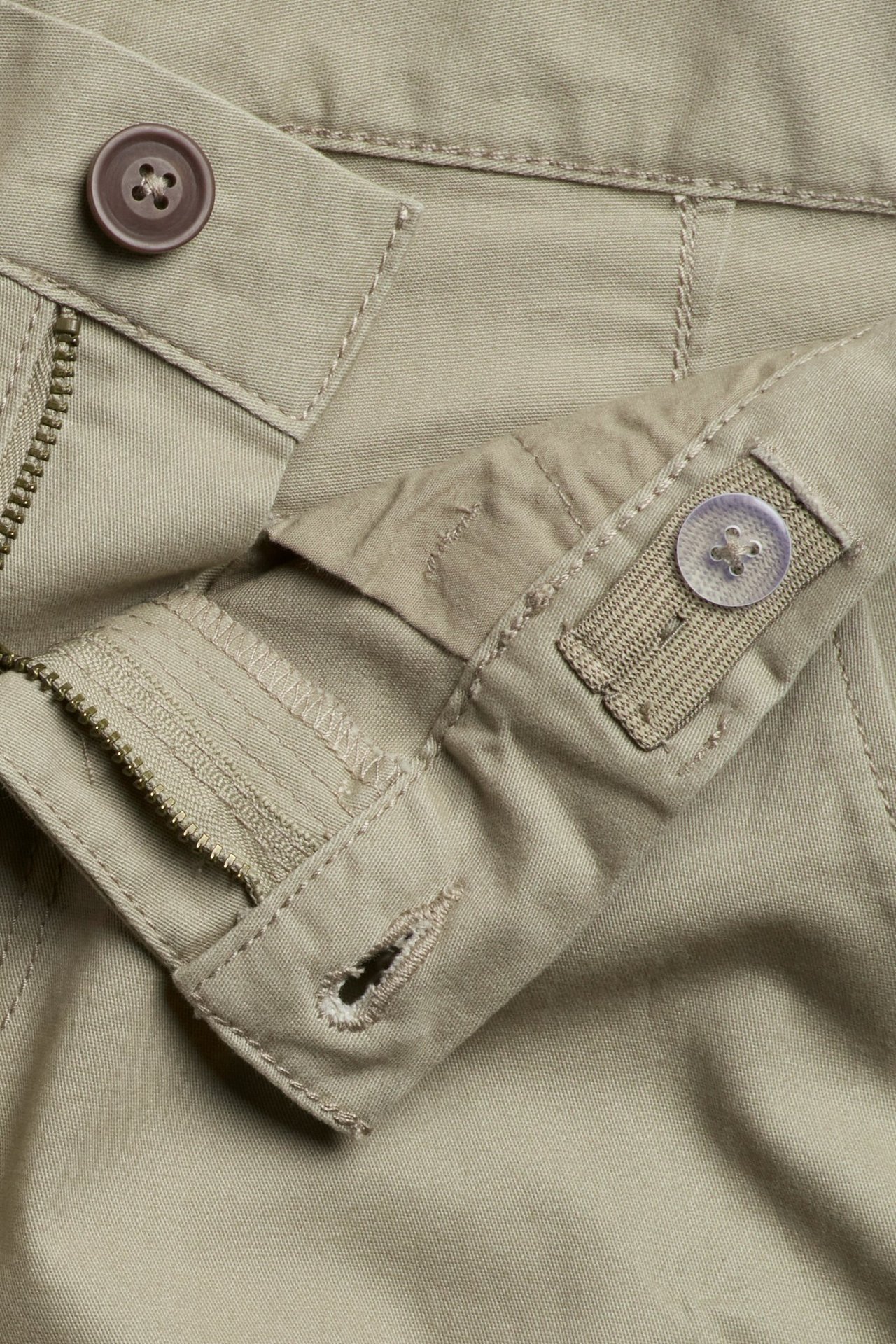 Lähikuva lasten khakinvihreistä chinoista, joissa ruskea nappi, vetoketju ja säädettävä joustovyötärö.