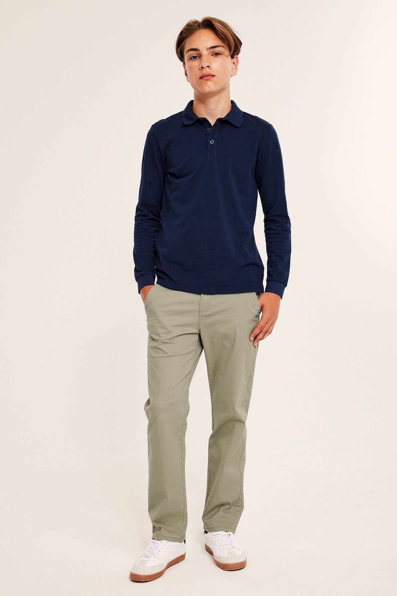 Mies tummansininen pikeepaita, beige chino-pantalonit, valkoiset lenkkarit, etunäkymä.