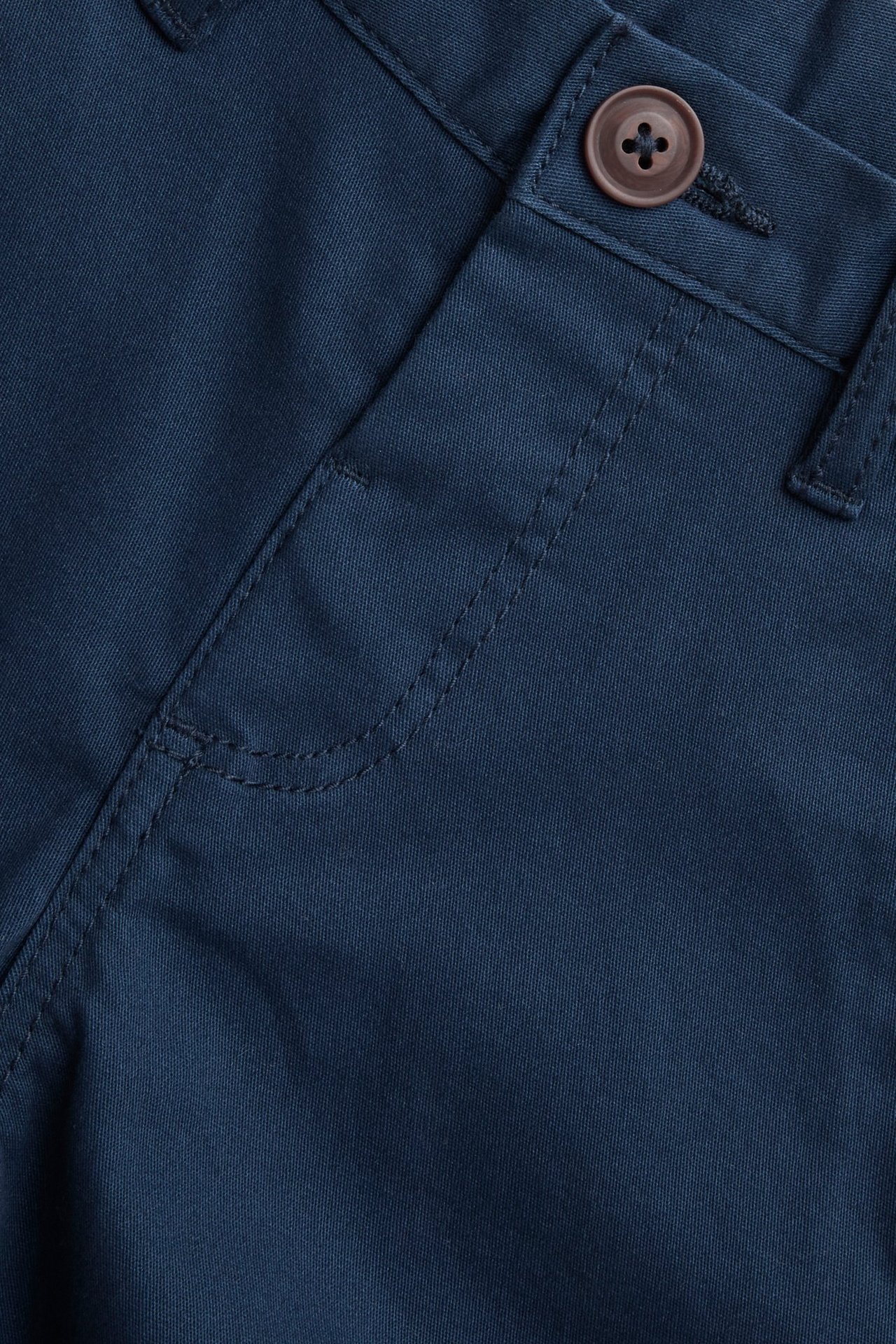 Zbliżenie na granatowe, elastyczne bawełniane chinosy dziecięce z brązowym guzikiem i imitacją rozporka.