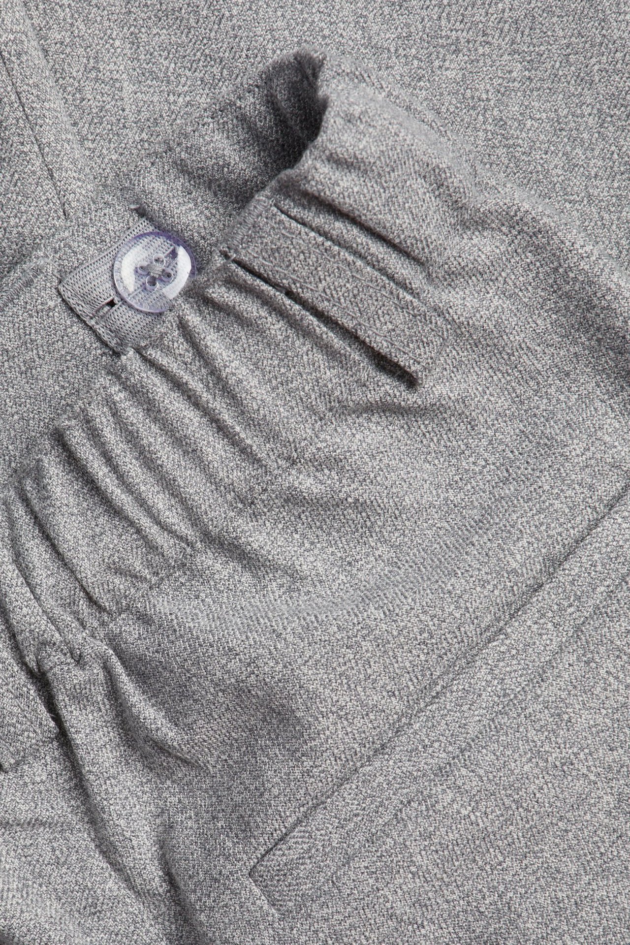 Zbliżenie na dziecięce jasnoszare spodnie melanżowe z elastycznym pasem i przezroczystym guzikiem.