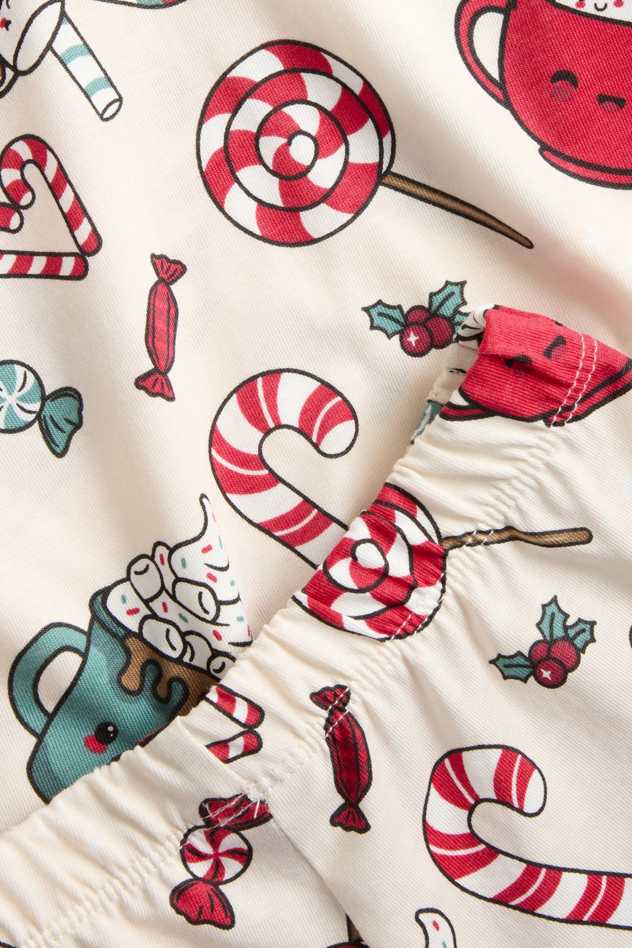 Närbild av ljusbeige barnpyjamas i bomull med festligt rött och vitt godistryck.