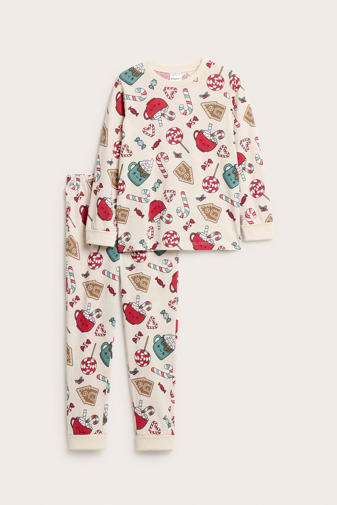 Edestä kuvattuna lasten vaaleabeiget puuvillapyjamat, jouluisella karkki- ja piparkakkukuviolla.