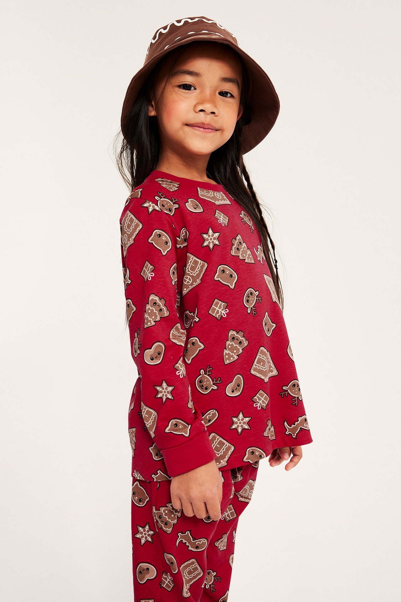 Jente i rød jul-pysjamas med pepperkake-mønster, hatt, profil.