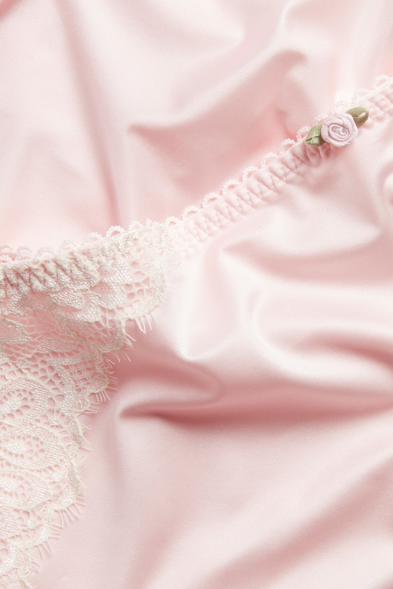 Zbliżenie na jasnoróżowe damskie figi z białą koronkową lamówką i małą różową różyczką.