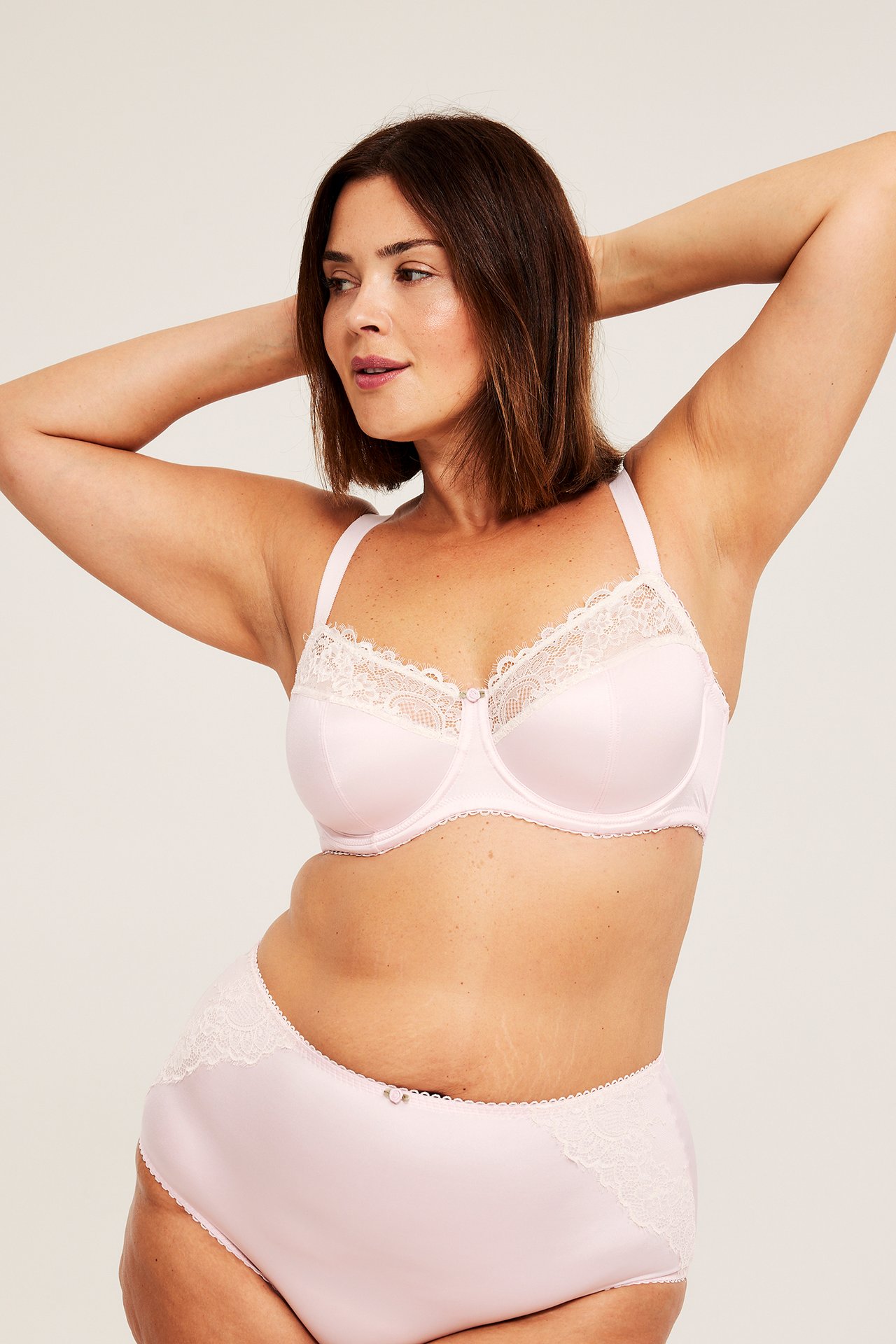 Edestäpäin, nainen yllään vaaleanpunaiset alushousut valkoisilla pitsiyksityiskohdilla ja yhteensopivat rintaliivit.
