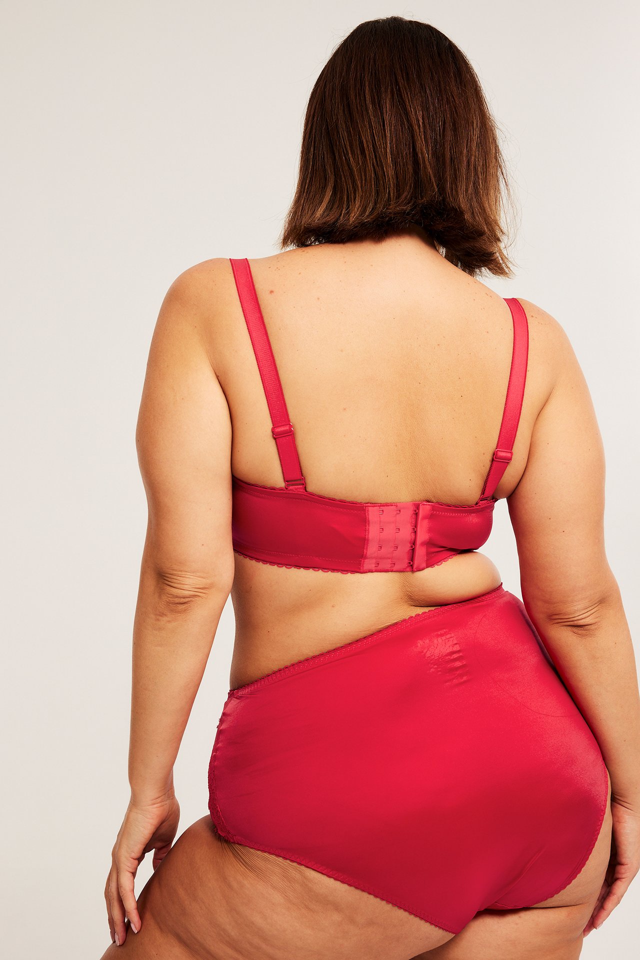 Naisen takaa, punaiset pitsikoristeiset brief-alushousut ja yhteensopivat rintaliivit hakasilla.