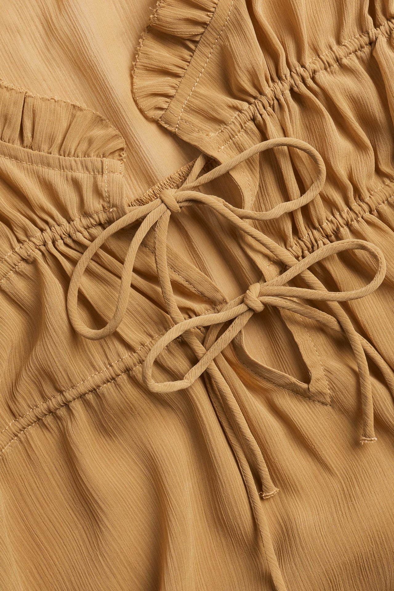 Zbliżenie beżowej bluzki poliestrowej z falbankowym dekoltem w serek i wiązanym sznurkiem.