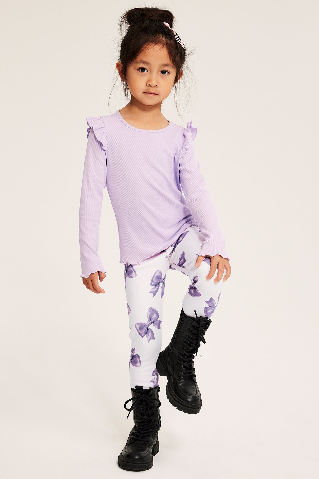 Tyttö vaaleanlilassa topissa, kuvioiduissa leggingseissä ja mustissa saappaissa.