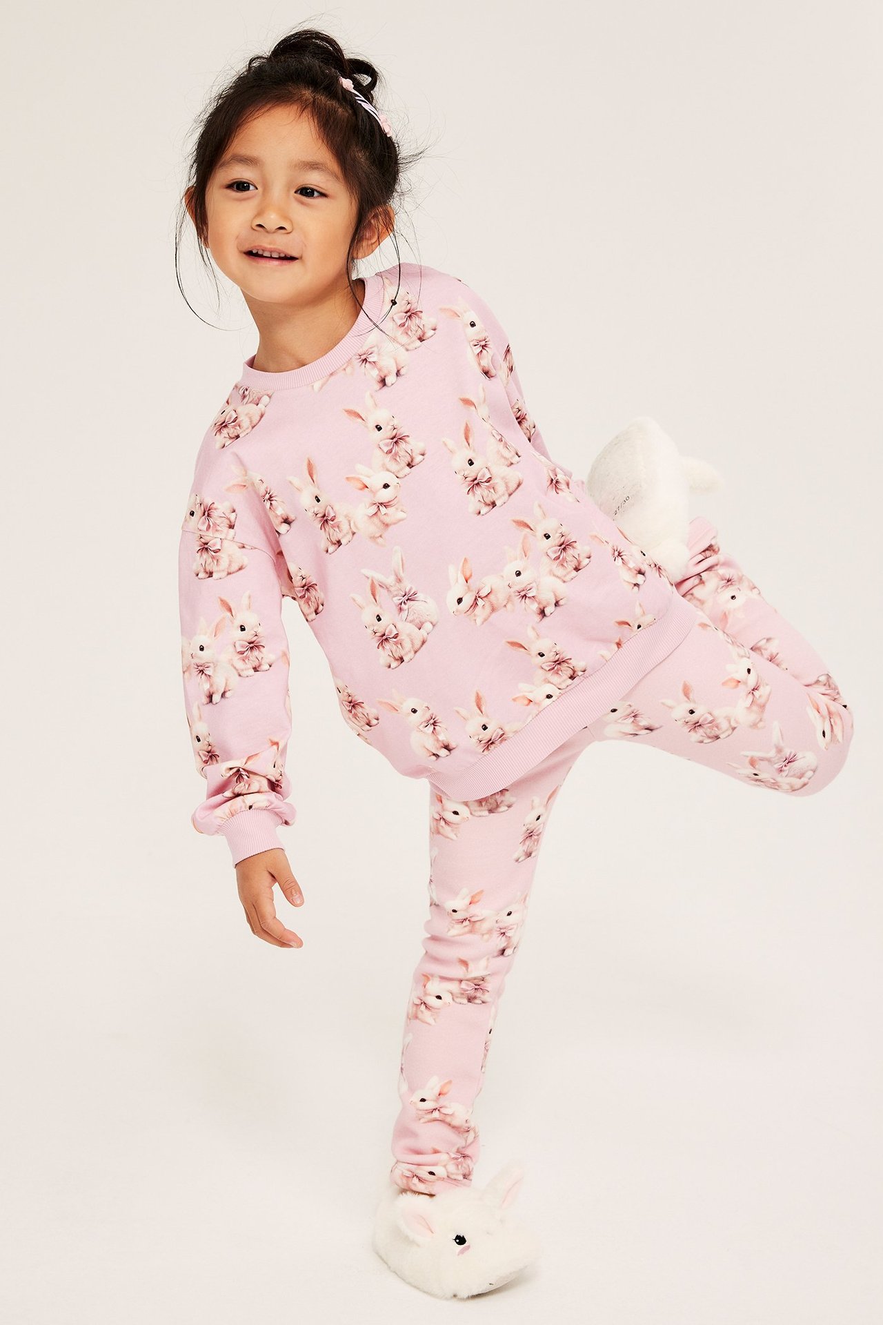 Tyttö pinkeissä pupukuvioisissa legginsissä ja yläosassa, seisoo yhdellä jalalla.