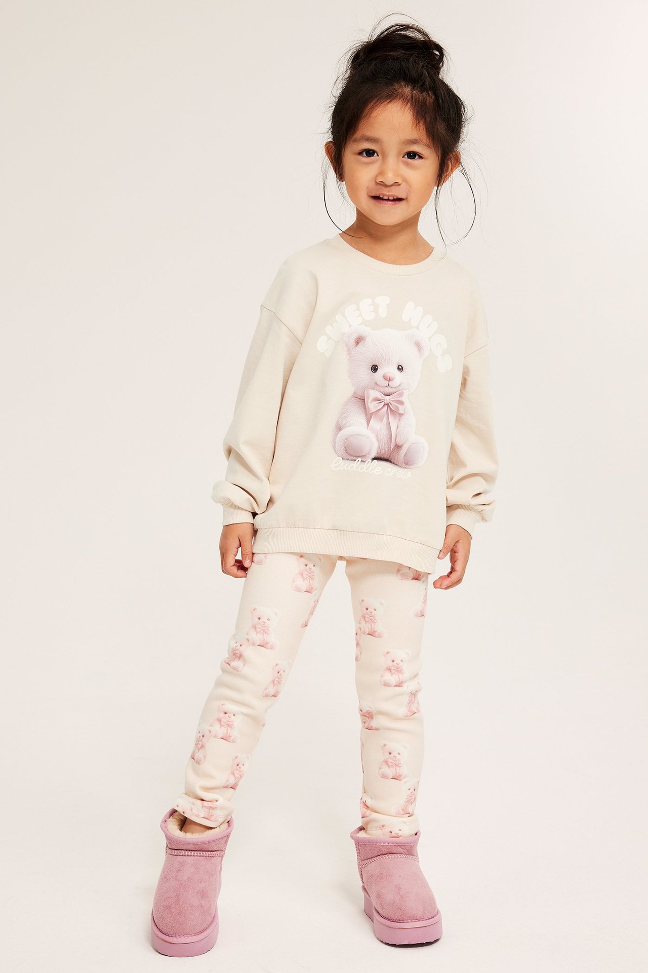 Pikkutyttö beigeissä collegepaidassa ja legginsseissä, rosa saappaat.