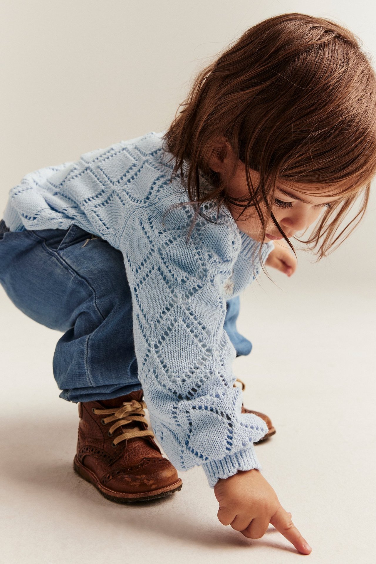 Närbild på ett barn i ljusblå mönsterstickad bomullskofta, blåa jeans och bruna kängor.