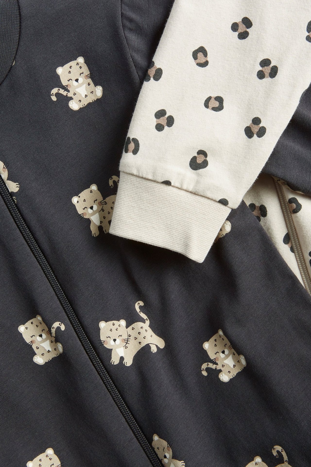 Zbliżenie na dwupak pajacyków dla niemowląt: jeden ciemnoszary z nadrukiem lamparta, jeden beżowy w cętki.