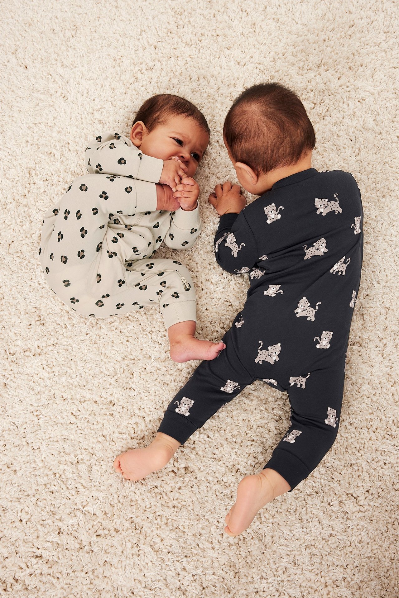 Widok z góry: Dwoje niemowląt w piżamach w panterkę. Jedna beżowa z dwukierunkowym zamkiem, druga granatowa.