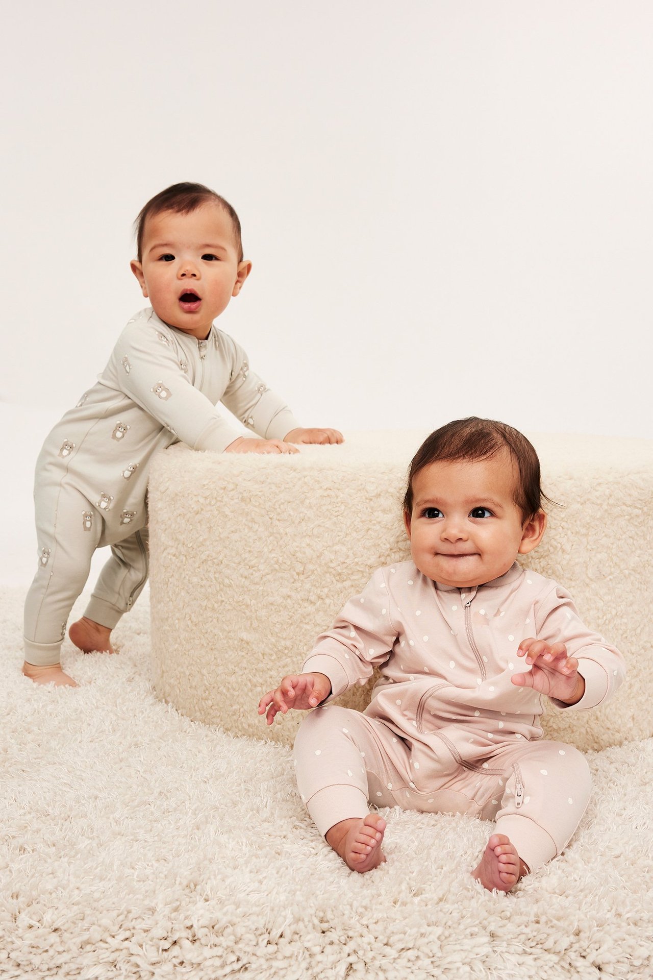 Dwa niemowlęta w pajacykach: jasnoróżowy w kropki, jasnobeżowy w zwierzęcy wzór, oba z dwukierunkowym zamkiem.
