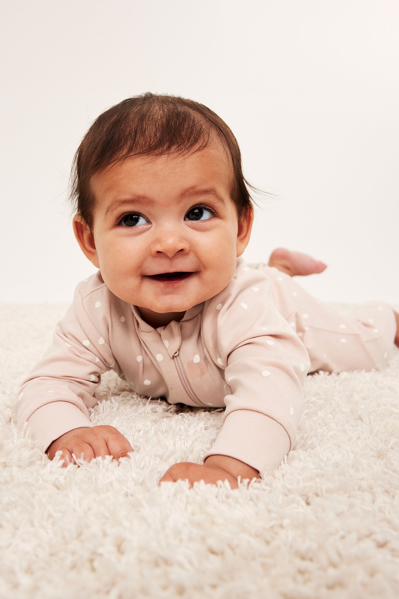 Widok z przodu: dziecko w jasnobeżowej piżamie we wzory z białymi kropkami i dwukierunkowym zamkiem.