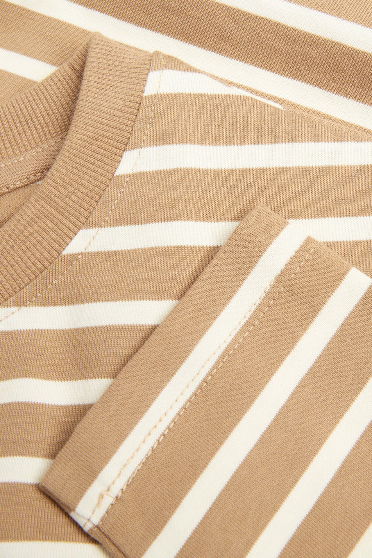 Zbliżenie beżowo-białej bluzki w paski z długim rękawem, wykonanej z grubego dżerseju, z prążkowanym dekoltem.