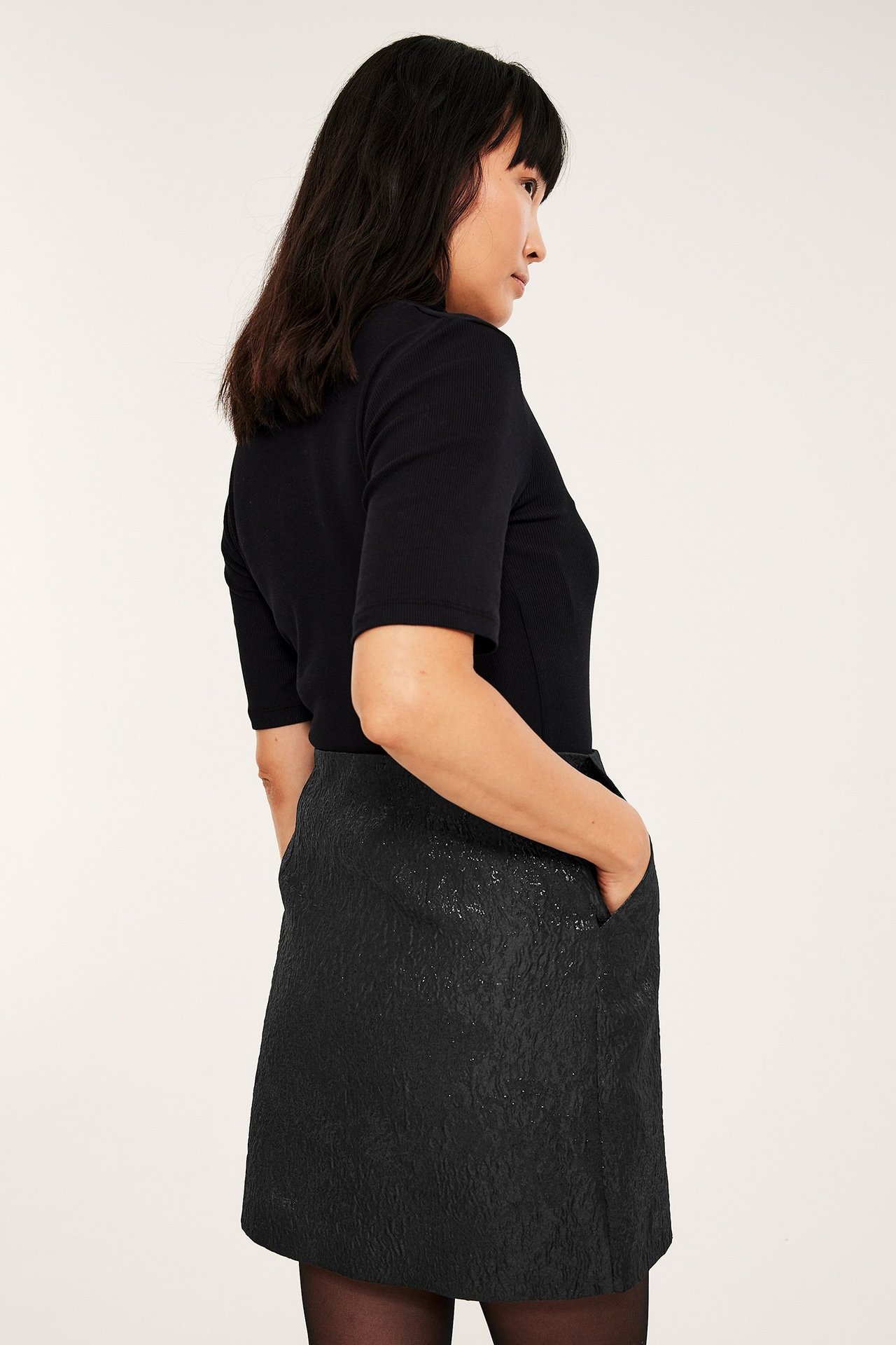 Kvinna iklädd svart brokadkjol med sidofickor och dragkedja, och matchande mörkblå blus.