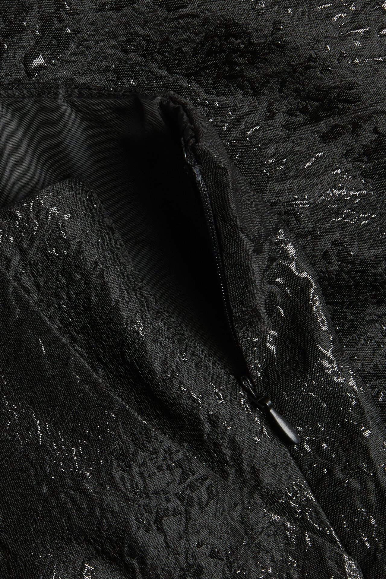 Zbliżenie czarnej spódnicy żakardowej o teksturowanym wzorze z widocznym zamkiem błyskawicznym.