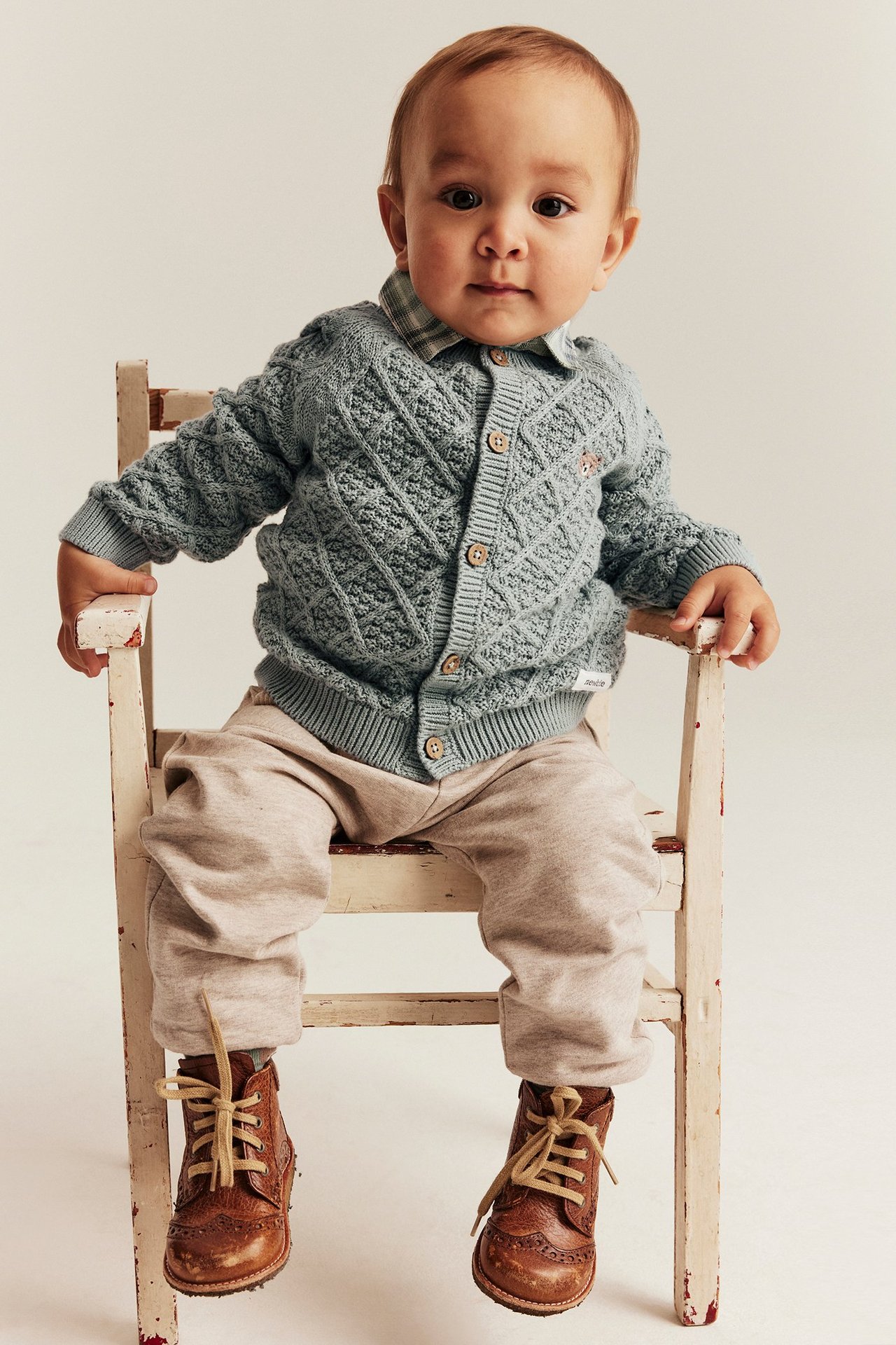 Widok z przodu: Niemowlę w jasnozielonym swetrze rozpinanym z rombami, drewniane guziki, koszula, beżowe spodnie, brązowe buty.