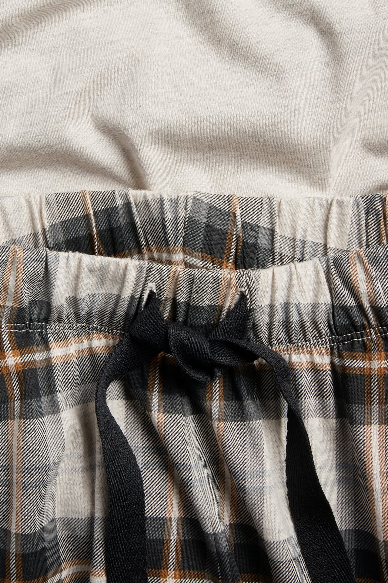 Närbild av beigerutiga pyjamasbyxor med svart dragsko i midjan, med en beigemelerad pyjamastopp.