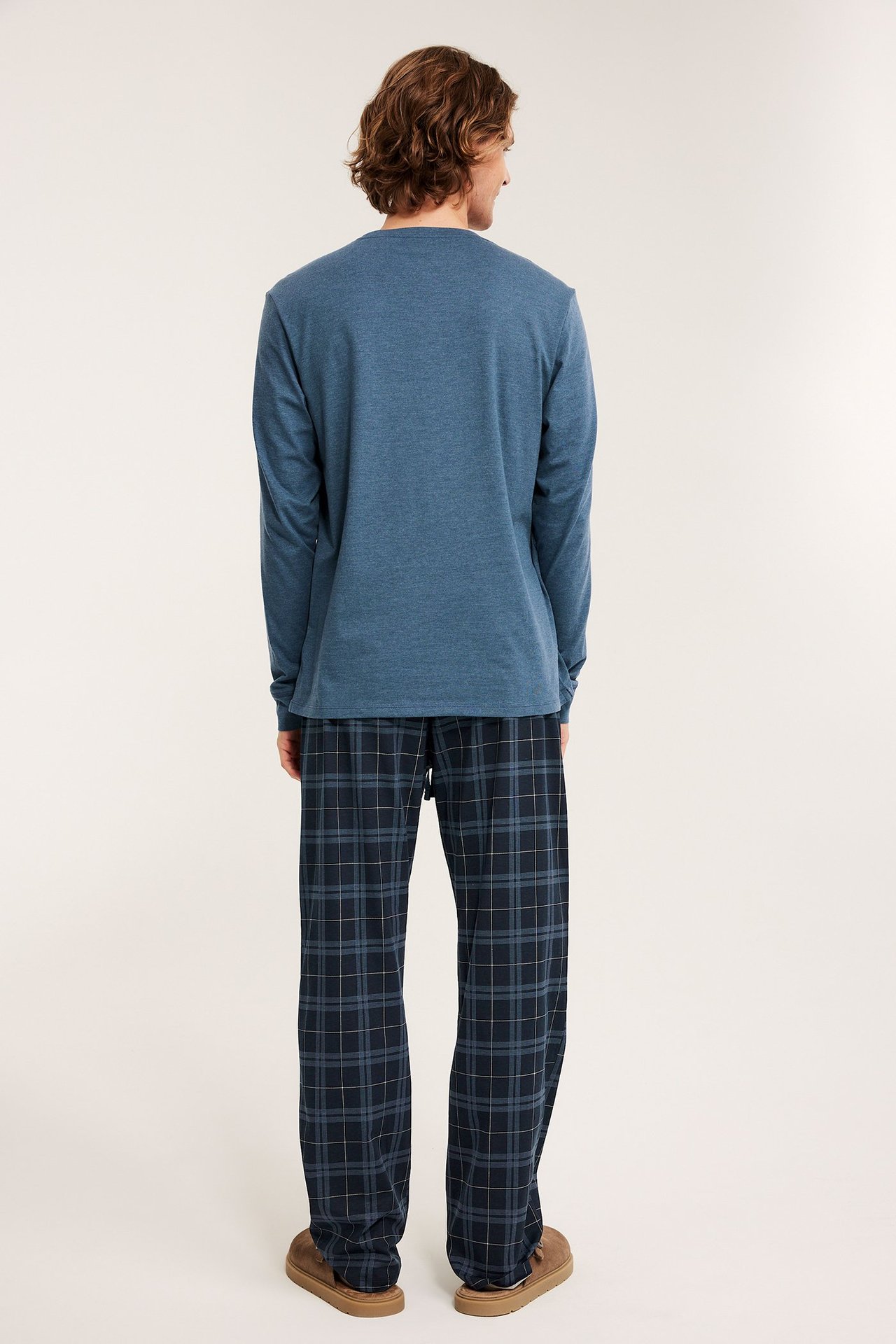 Ryggvy av en man i en blå långärmad pyjamaströja och mörkblå rutiga pyjamabyxor.