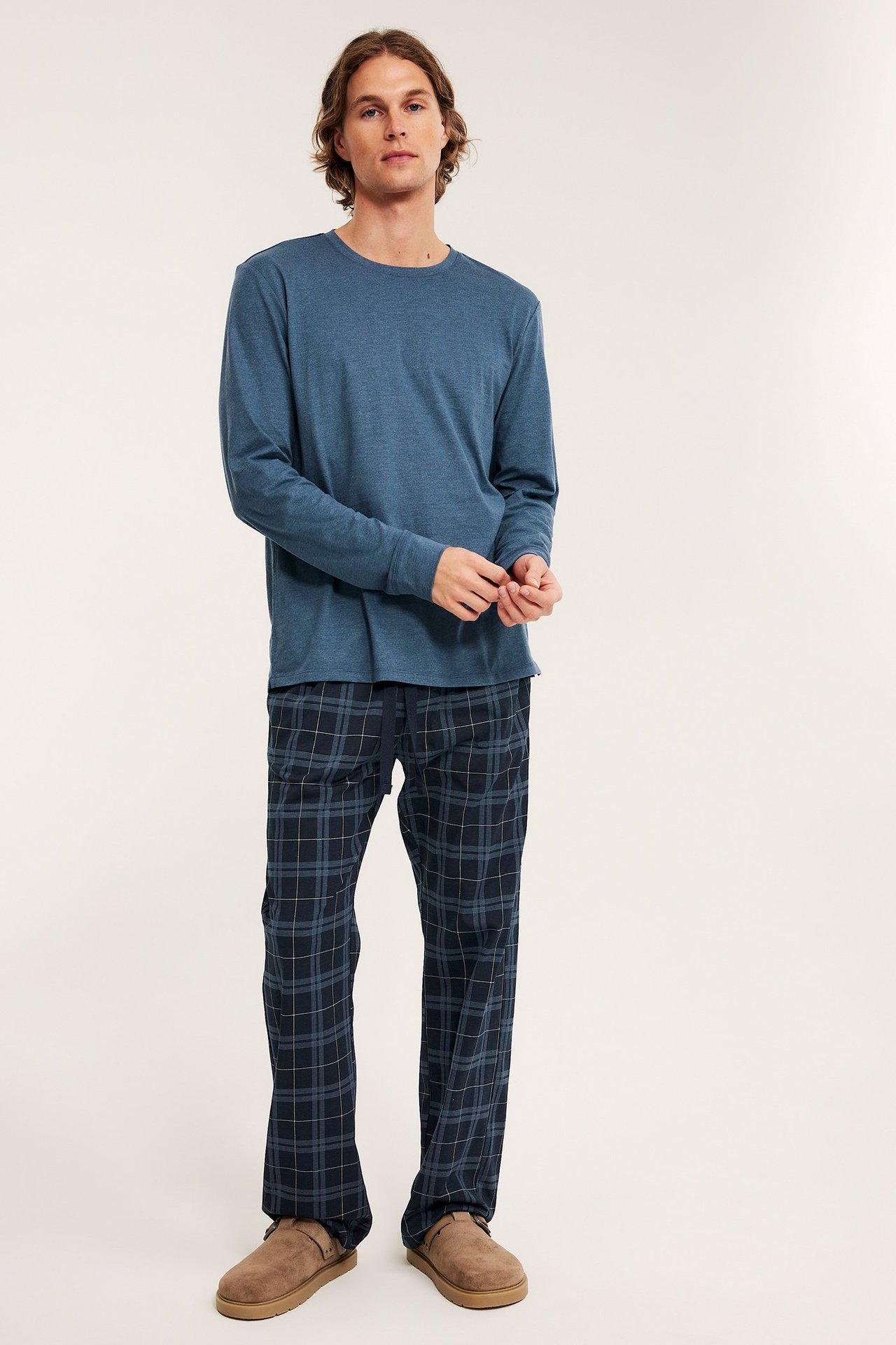 Mies edestäpäin: sininen pitkähihainen pyjamapaita, tummansiniset ruudulliset pyjamahousut ja ruskeat tohvelit.