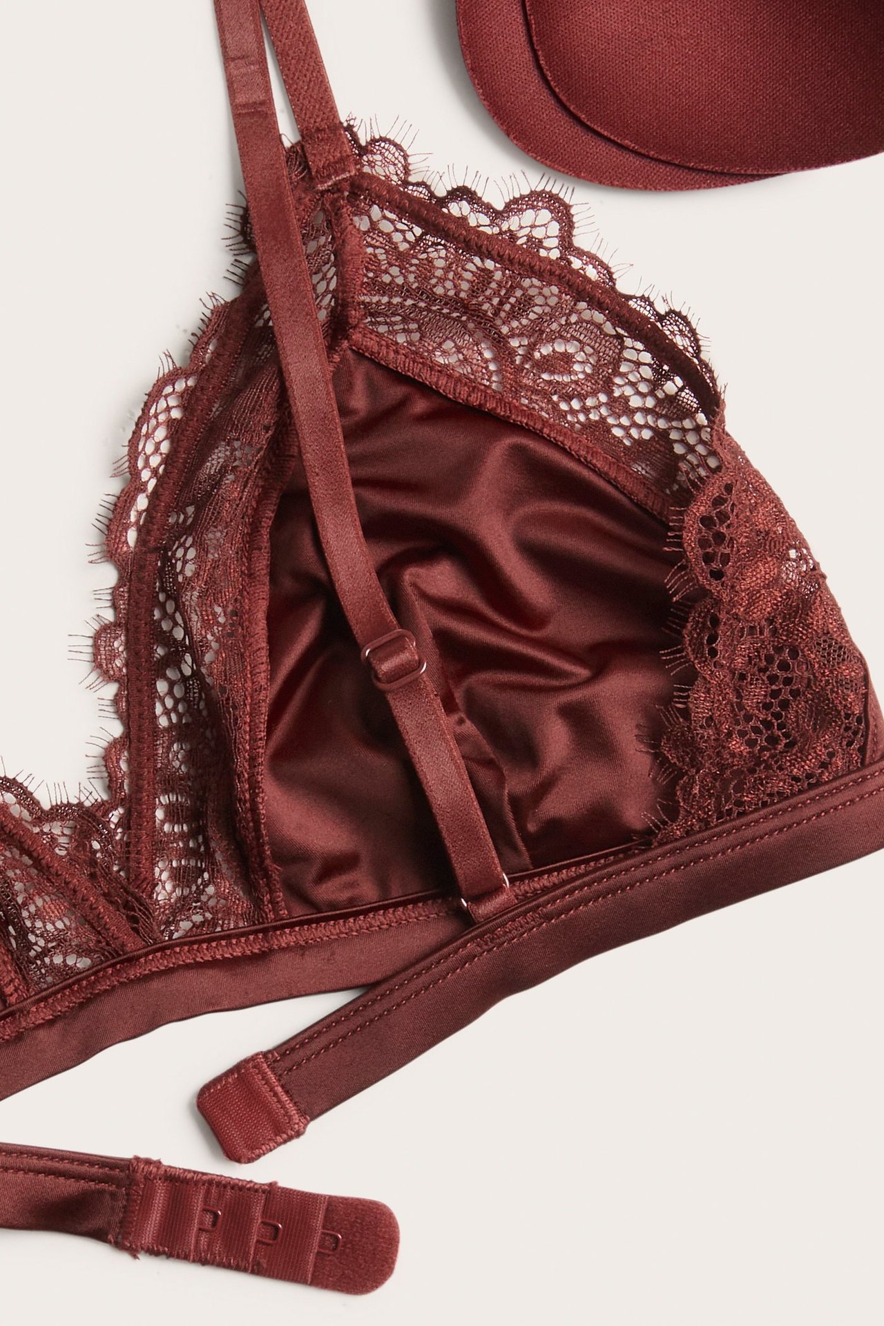 Zbliżenie na ciemnoczerwoną wyściełaną braletkę z satynowymi miseczkami, koronkowym wykończeniem, regulowanymi ramiączkami i zapięciem.
