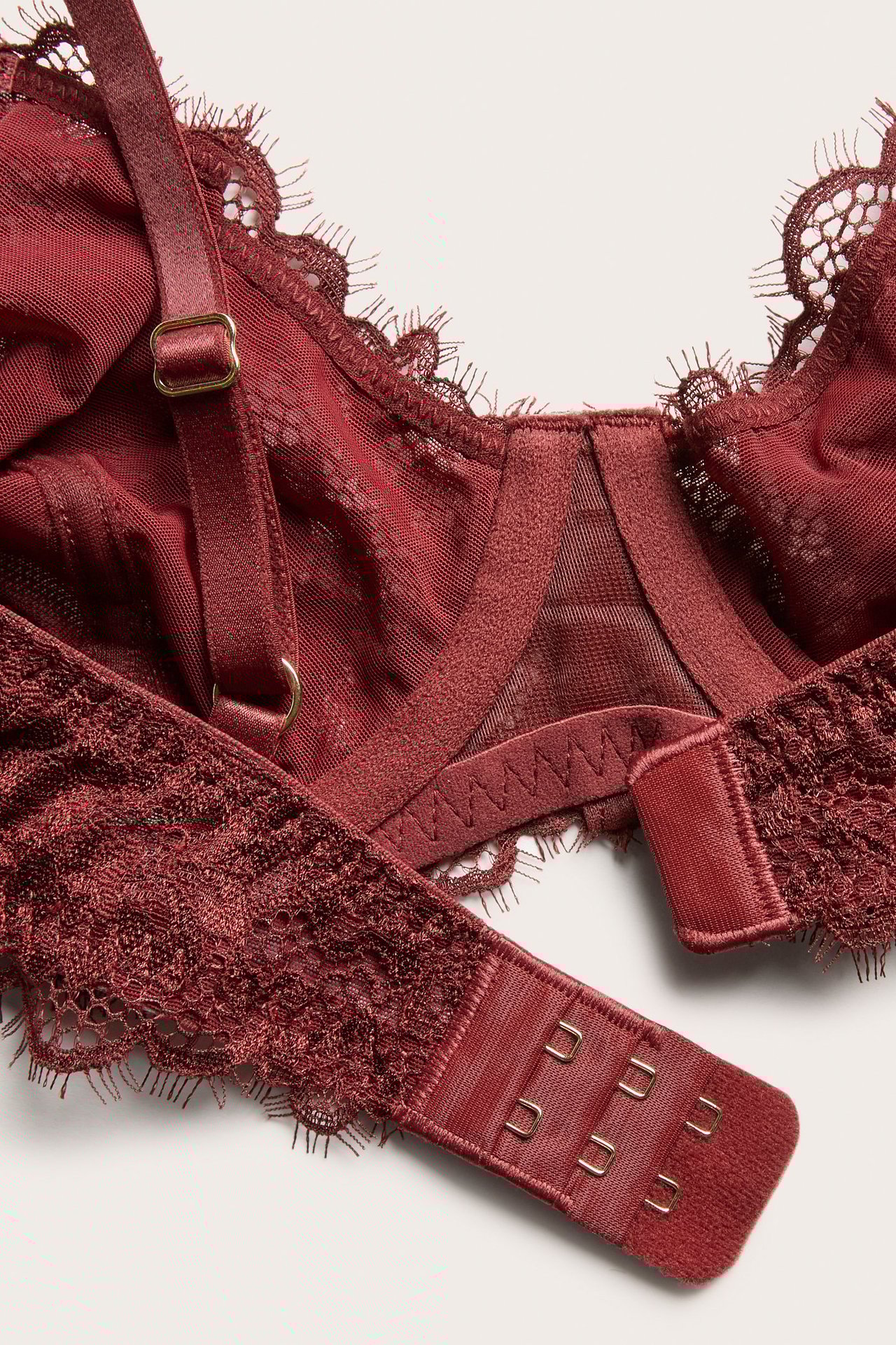 Nærbilde av en rød blonde-BH med spiler, justerbare stropper og hektelukking bakpå.