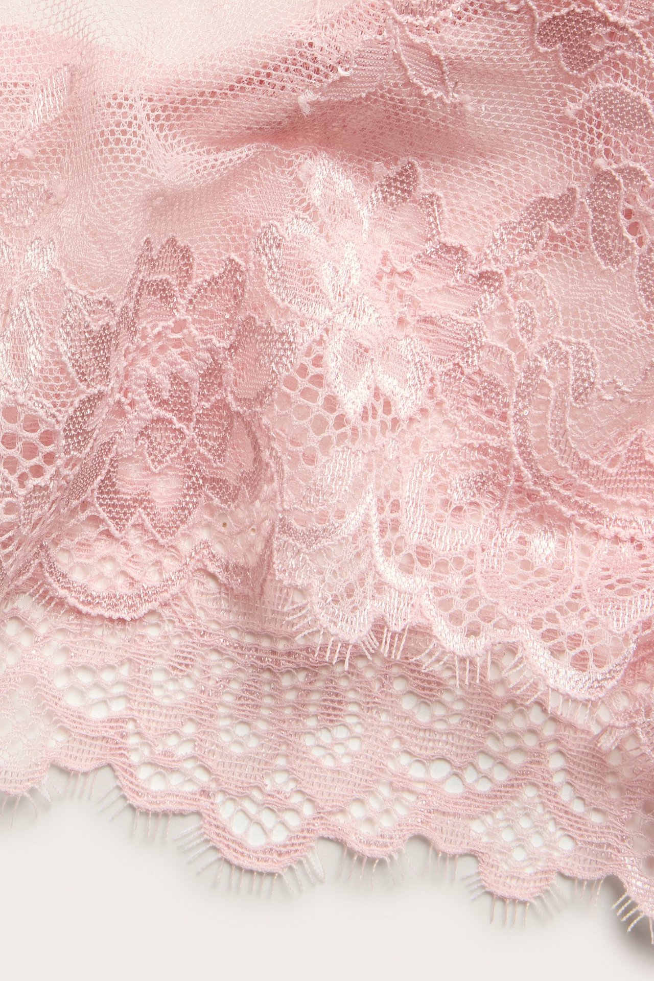 Zbliżenie na jasnoróżowe koronkowe figi cheeky z delikatnym rzęsowym brzegiem.