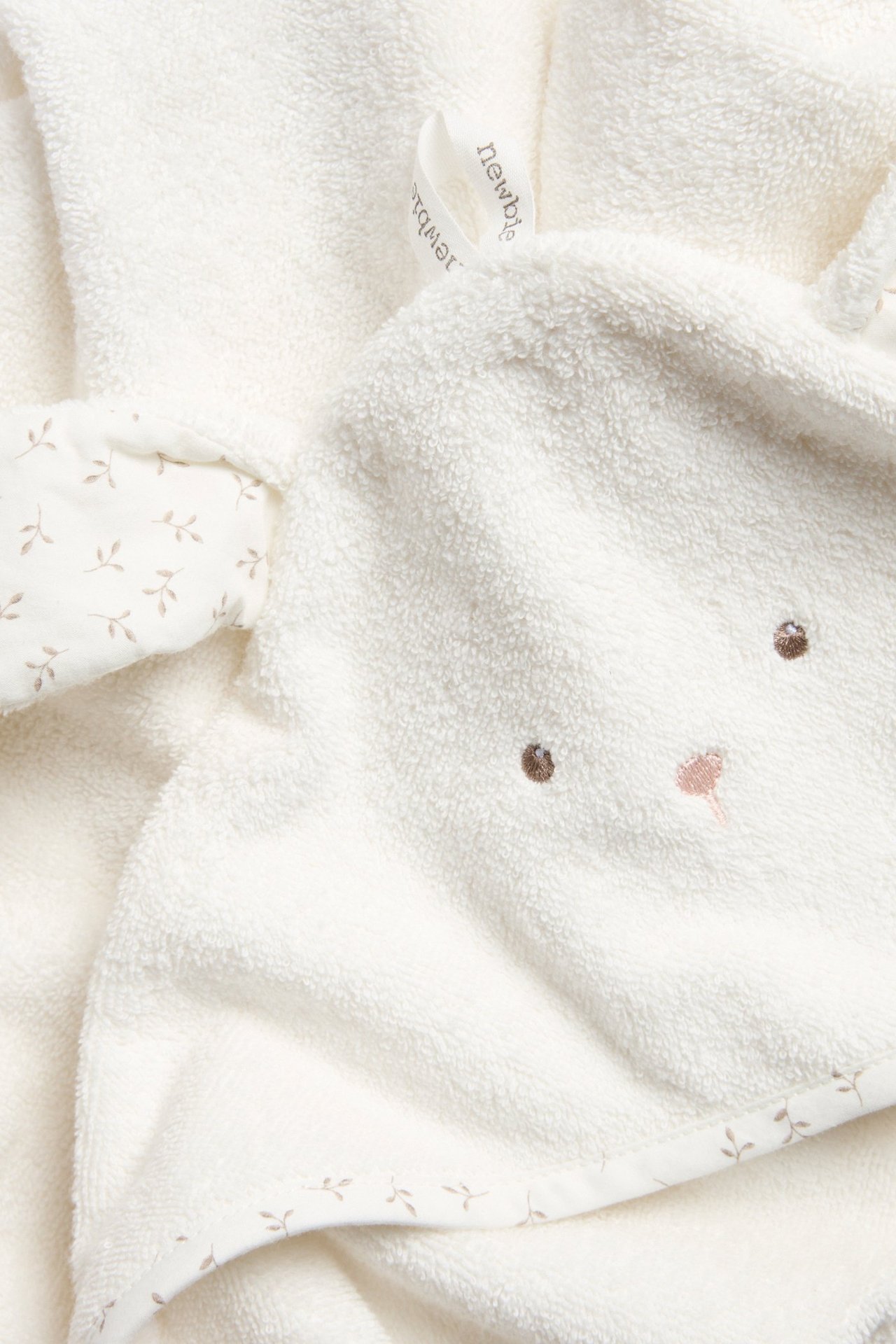 Närbild av en offwhite frottéhandduk med kaninöron, broderat ansikte och mönstrad kant för baby.