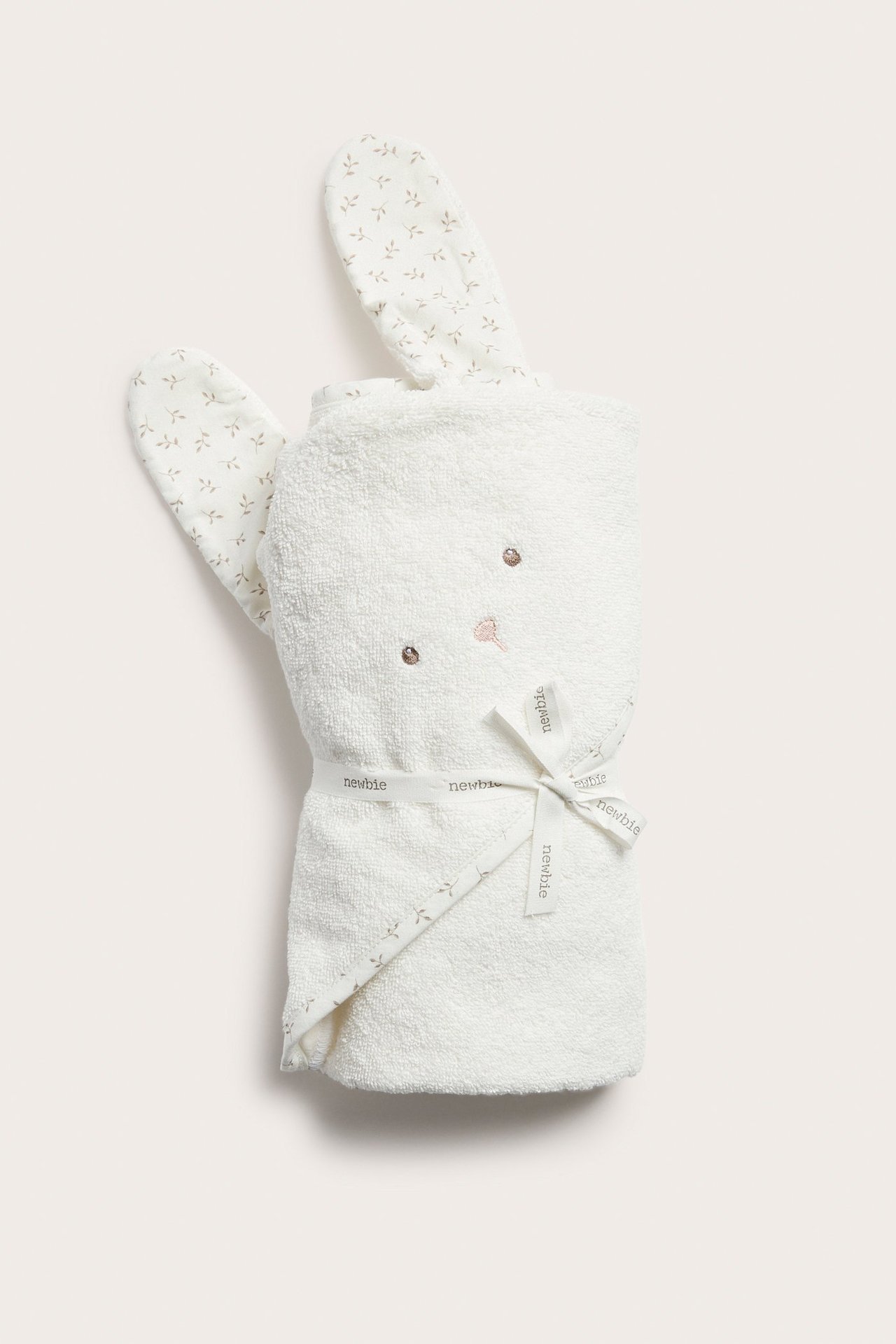 Framifrån: Offwhite bomullsfrotté badlakan med huva för baby, broderat kaninansikte, mönstrade öron, knutet med band.