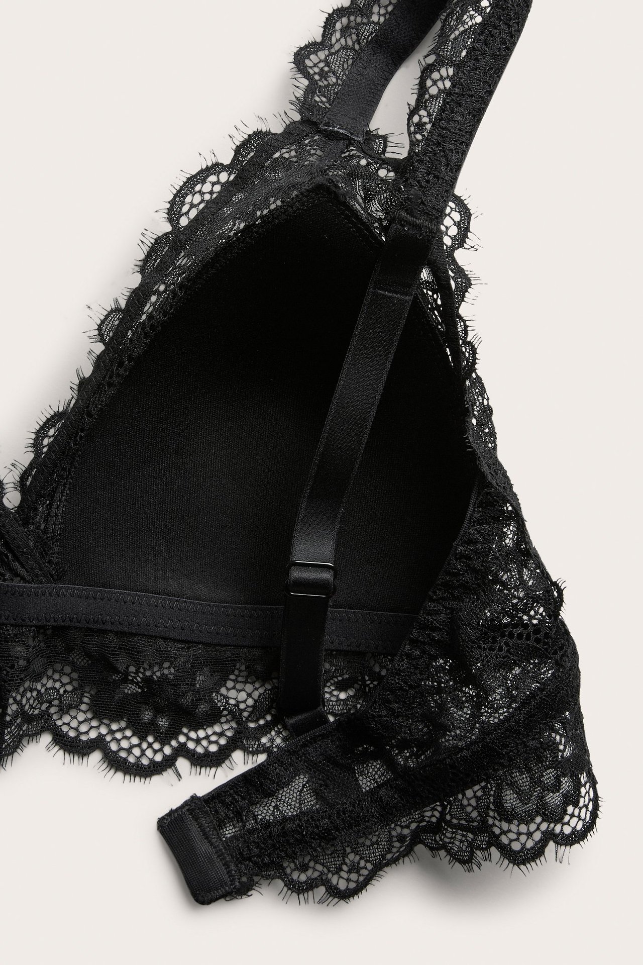 Zbliżenie czarnej, koronkowej braletki z wyściełanymi miseczkami, regulowanymi ramiączkami i zapięciem.