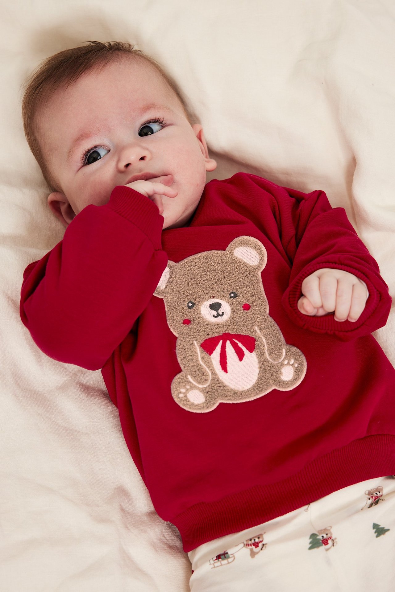 Nærbilde av baby i rød sweatshirt med bjørneapplikasjon og trykk foran.