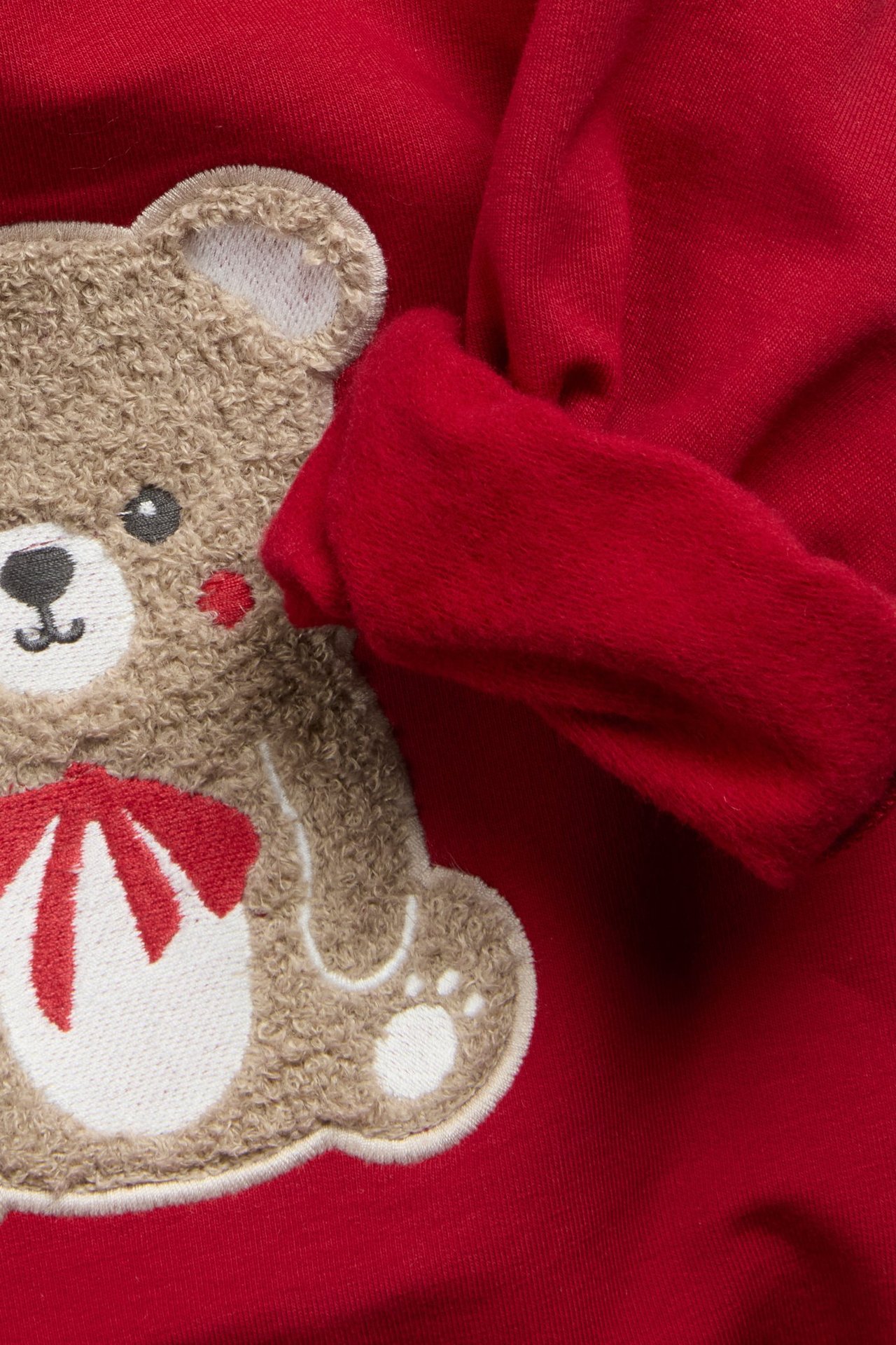 Zbliżenie na czerwoną bluzę dziecięcą z brązową aplikacją misia frotte trzymającego laskę cukrową.