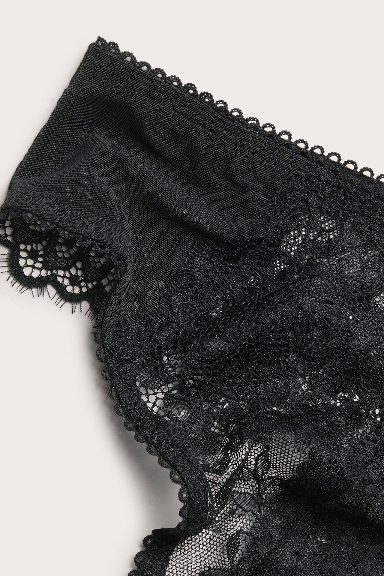 Zbliżenie czarnych koronkowych stringów z delikatnymi kwiatowymi wzorami i falowanymi brzegami.