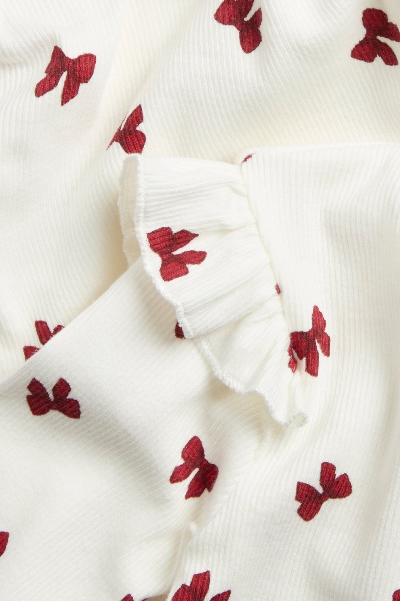 Zbliżenie na kremowe prążkowane body niemowlęce z czerwonym wzorem kokardek i falbanką.