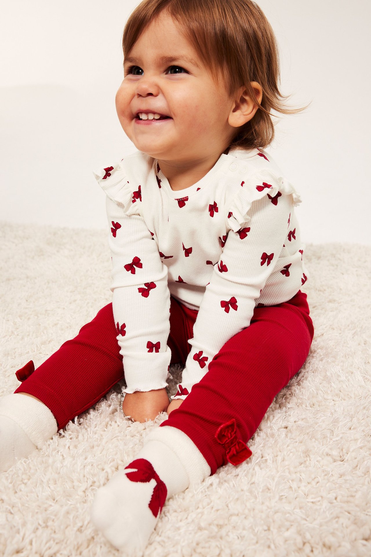 Offwhite ribbet babybody med rosetter, knapper på skulder og grop, mønstret.