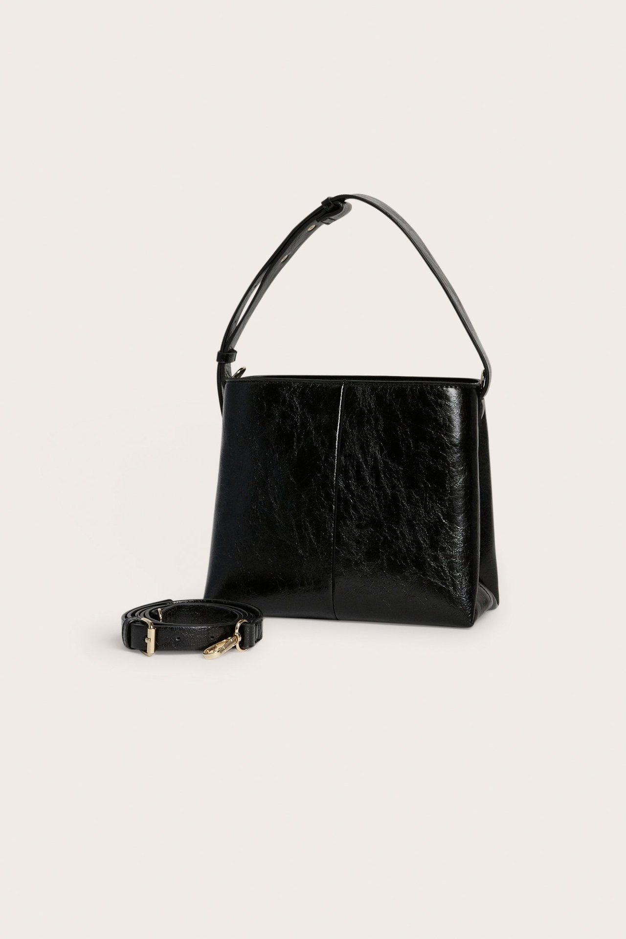 Edestä näkymä mustasta tekonahkaisesta käsilaukusta, jossa on lyhyt kahva ja irrotettava olkahihna.