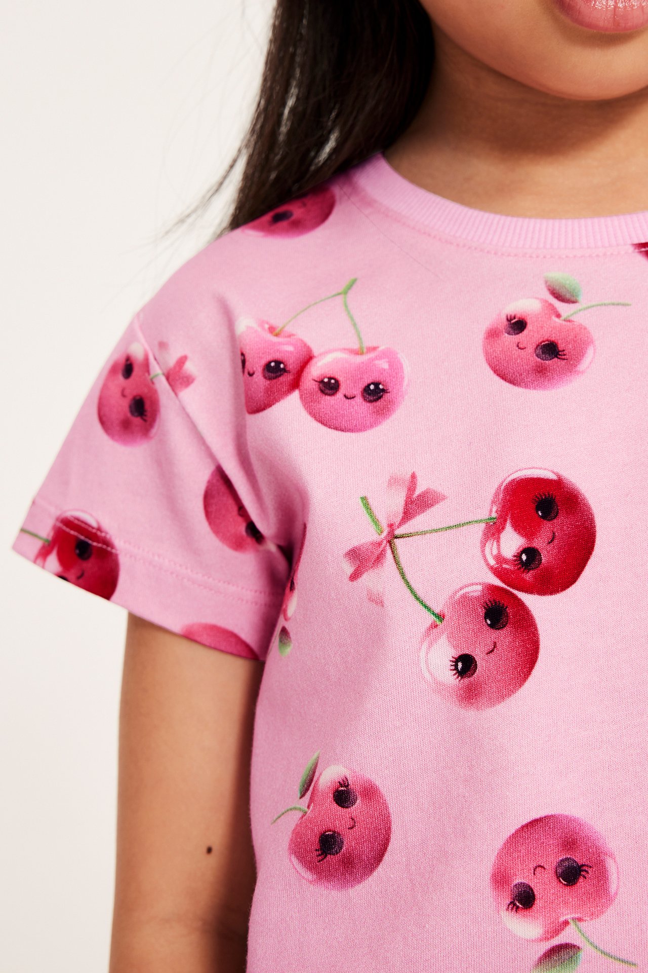 Närbild på ett barn i en rosa bomulls-t-shirt med lekfullt körsbärstryck.