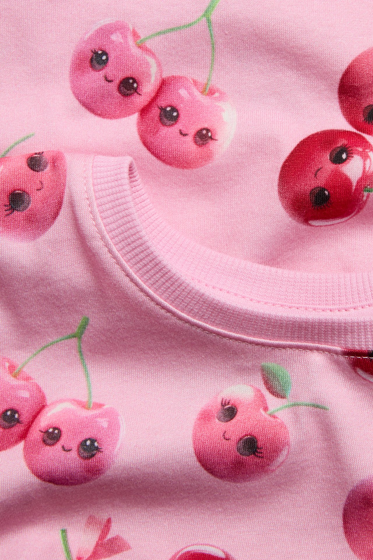Närbild av en rosa bomulls-t-shirt med mönstrat tryck av söta körsbär och ribbad halslinning.