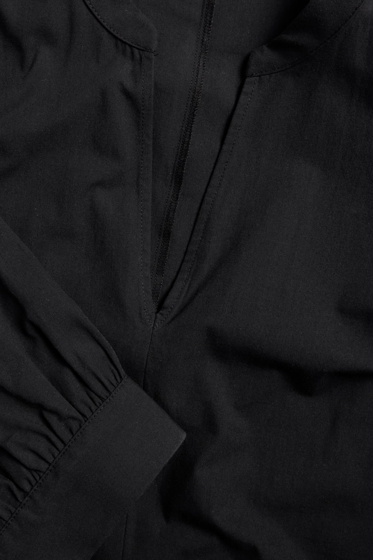 Zbliżenie czarnej krótkiej sukienki z popeliny bawełnianej z dekoltem w serek i marszczonym rękawem.