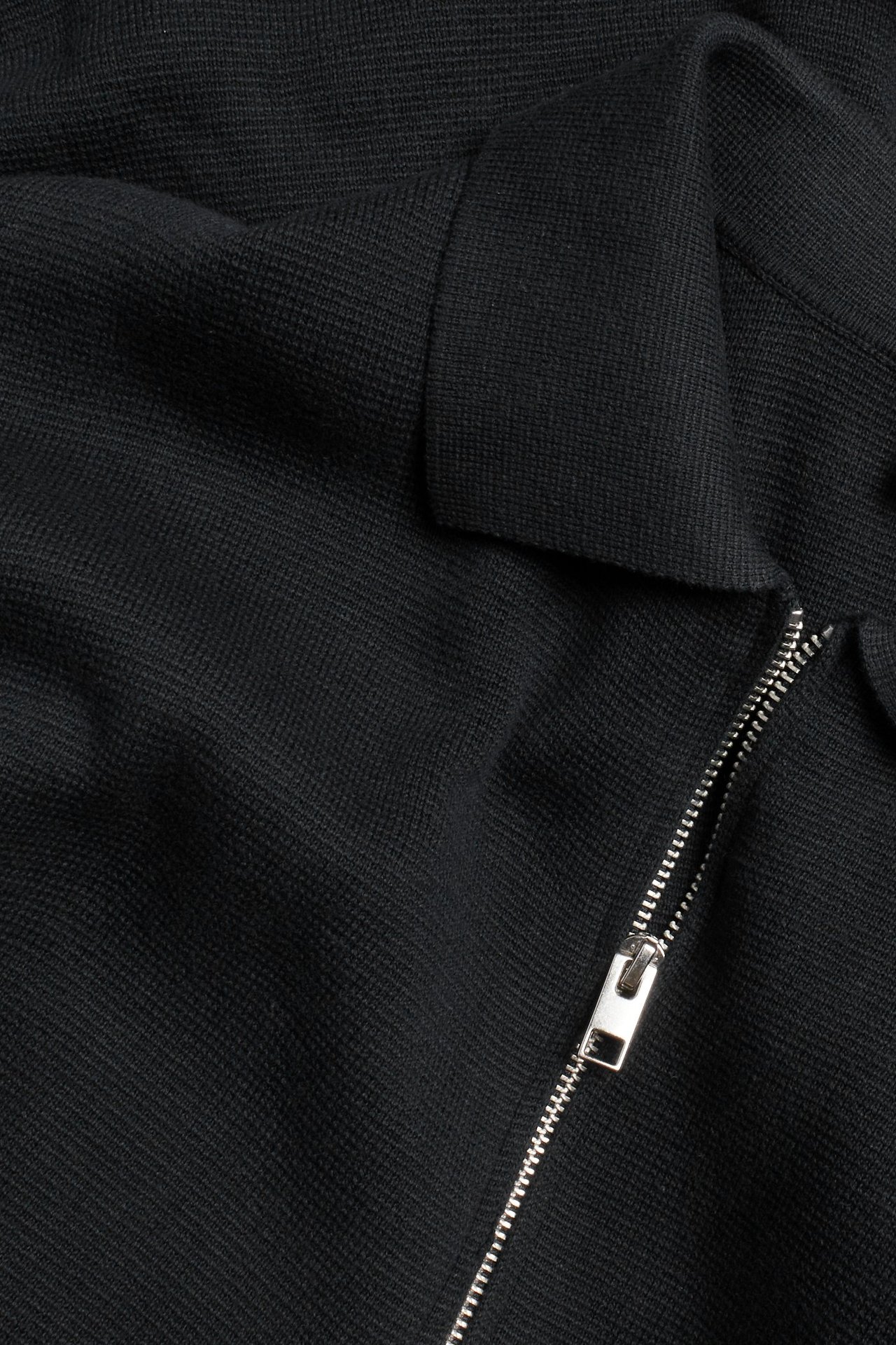 Zbliżenie czarnego bawełnianego swetra z dzianiny z srebrnym zamkiem błyskawicznym i kołnierzem.