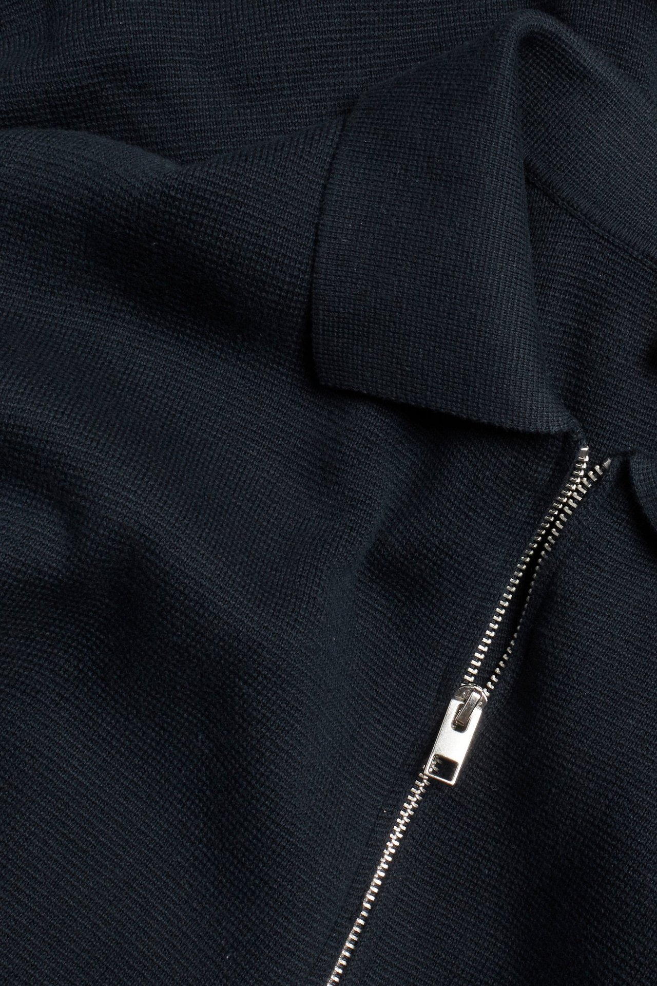 Zbliżenie na granatowy dzianinowy sweter bawełniany ze srebrnym zamkiem błyskawicznym.