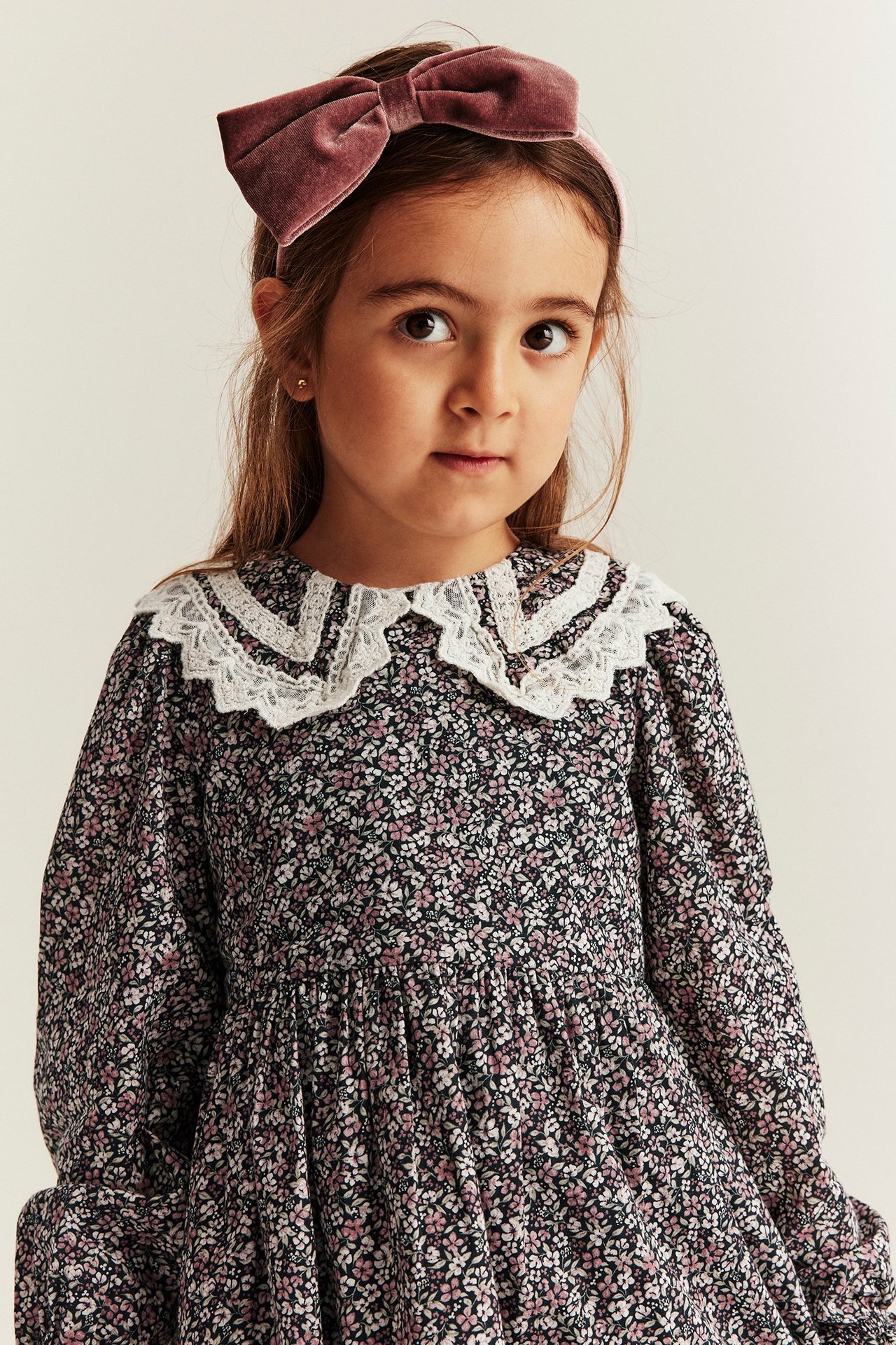 Nærbilde av et barn i en svart blomsterkjole med hvit blondekrage og et rosa fløyelsdiadem.