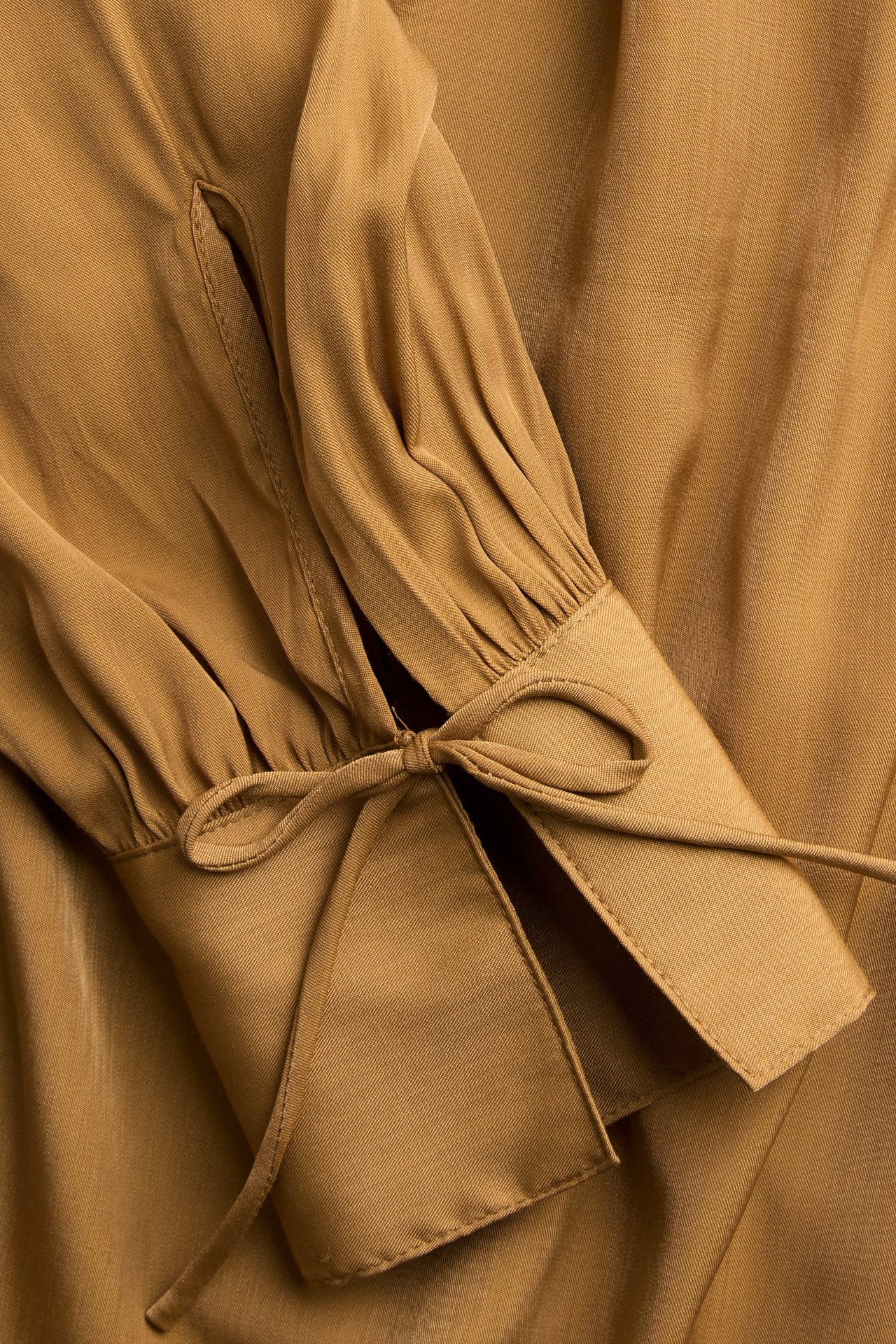 Lähikuva beigestä pitkähihaisesta puserosta, jossa on solmuyksityiskohta rypytetyssä hihansuussa.