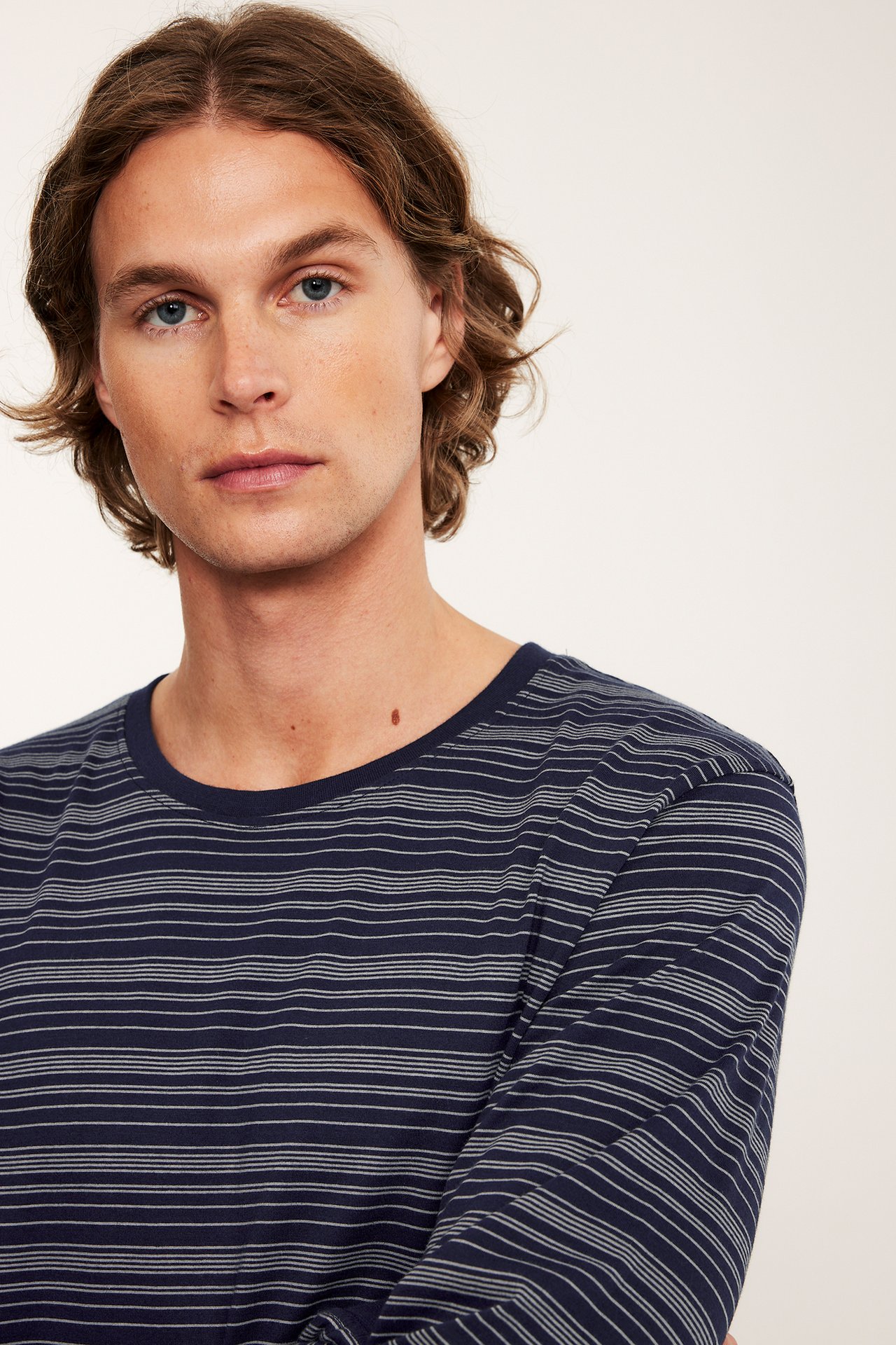 Nærbilde av en mann i en mørkeblå stripet bomulls pysjamastopp med lange ermer.